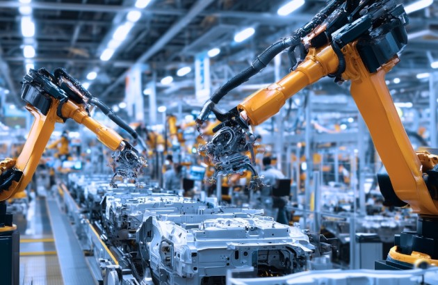 Anlagen-Maschinen-Seitenansicht von Robotern, die parallel an einem Fließband arbeiten, auf dem Fahrzeuginnenausstattungen hergestellt werden, mit orangefarbenen Roboterarmen und konzentrierten Arbeitern Seite an Seite