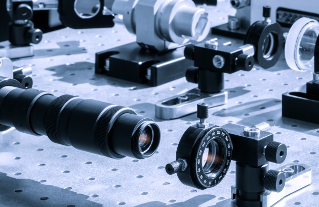 Optik- Optische Geräte, darunter ein Teleskop und Linsen, sind auf einem Tisch in einem Labor ausgestellt. Wissenschaftliches Experiment zum Thema Optik und Photonik mit Laserhintergrund
