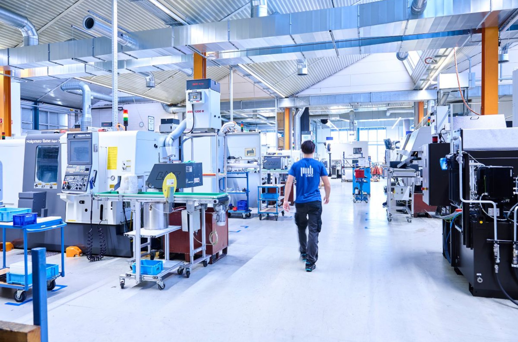 Mann läuft durch eine Produktionshalle mit Maschinen der CNC Fertigung auf ein Fenster zu