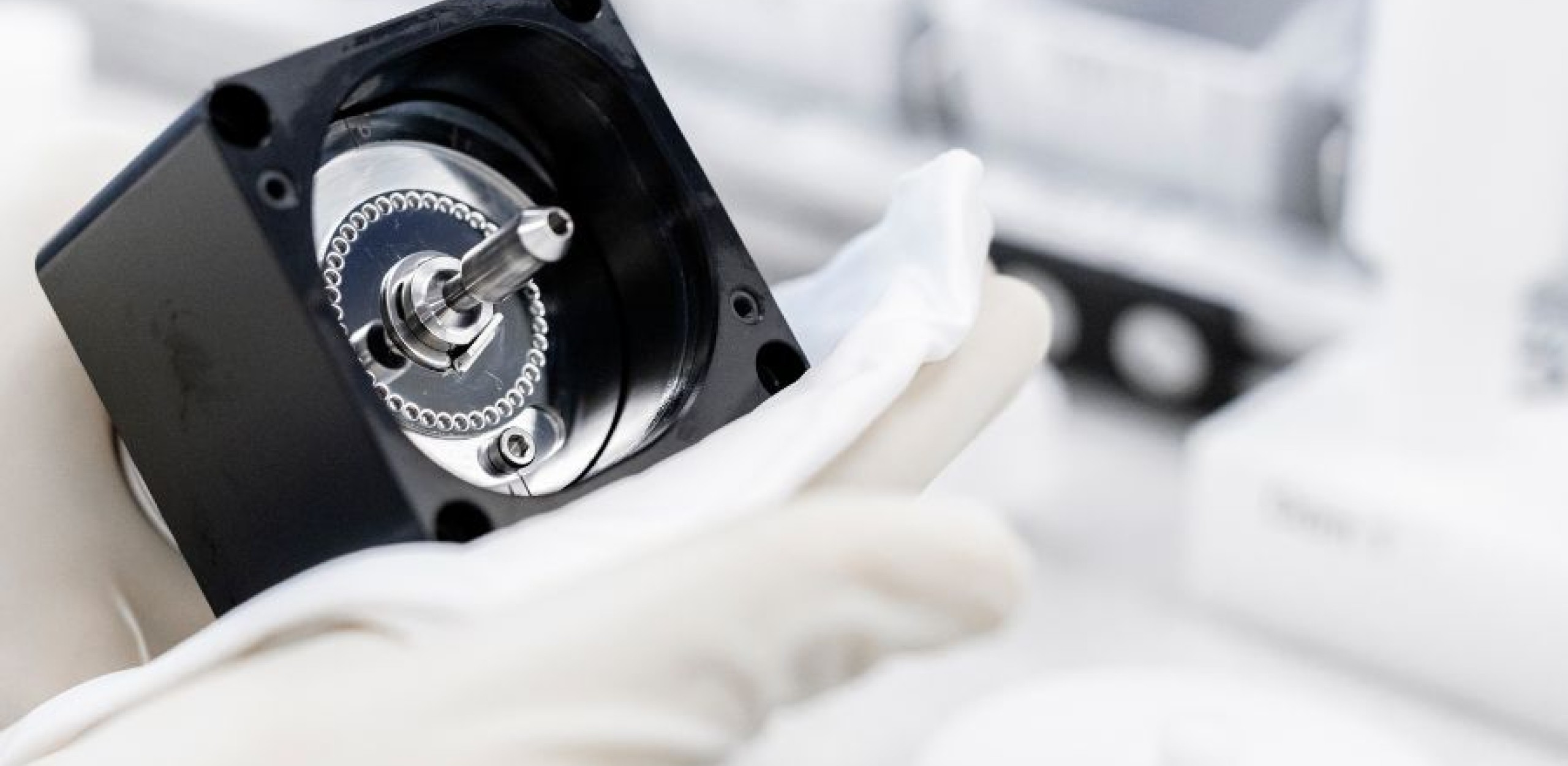 Zwei Hände in weissen Handschuhen halte ein Bauteil hoch und säubern es mit einem weissen Tuch