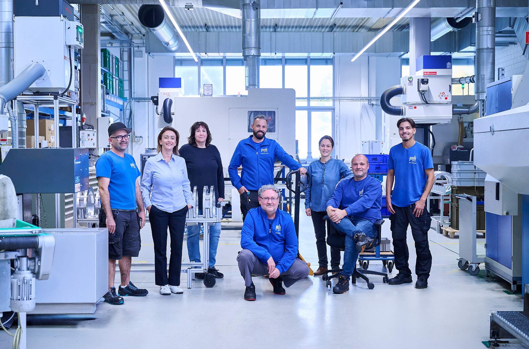 Mehrere Personen stehen in einer Produktionshalle für mechanische Fertigungsteile im Hintergrund sind CNC Maschinen zu sehen